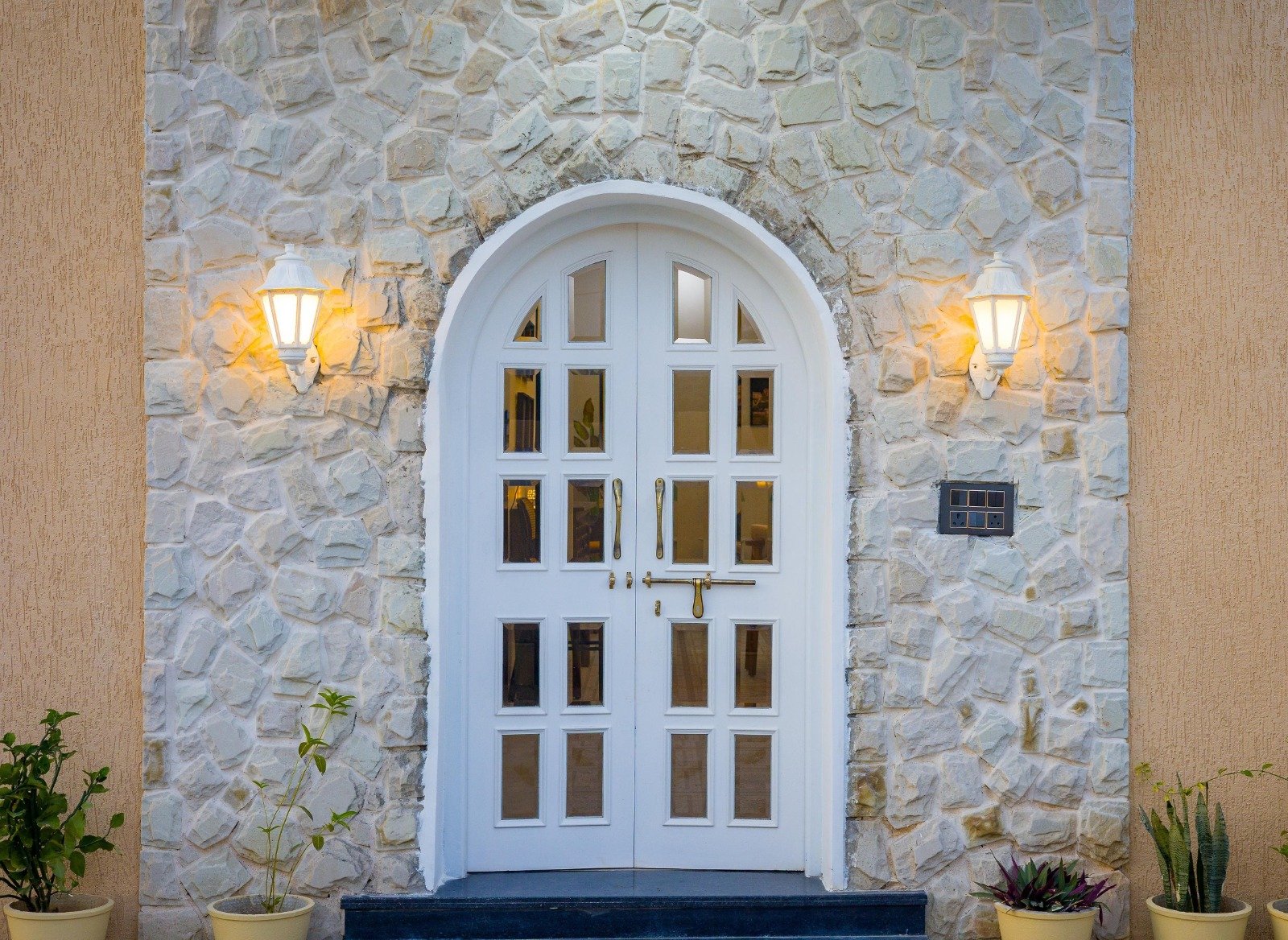 White arched door with glass panes and stone facade.