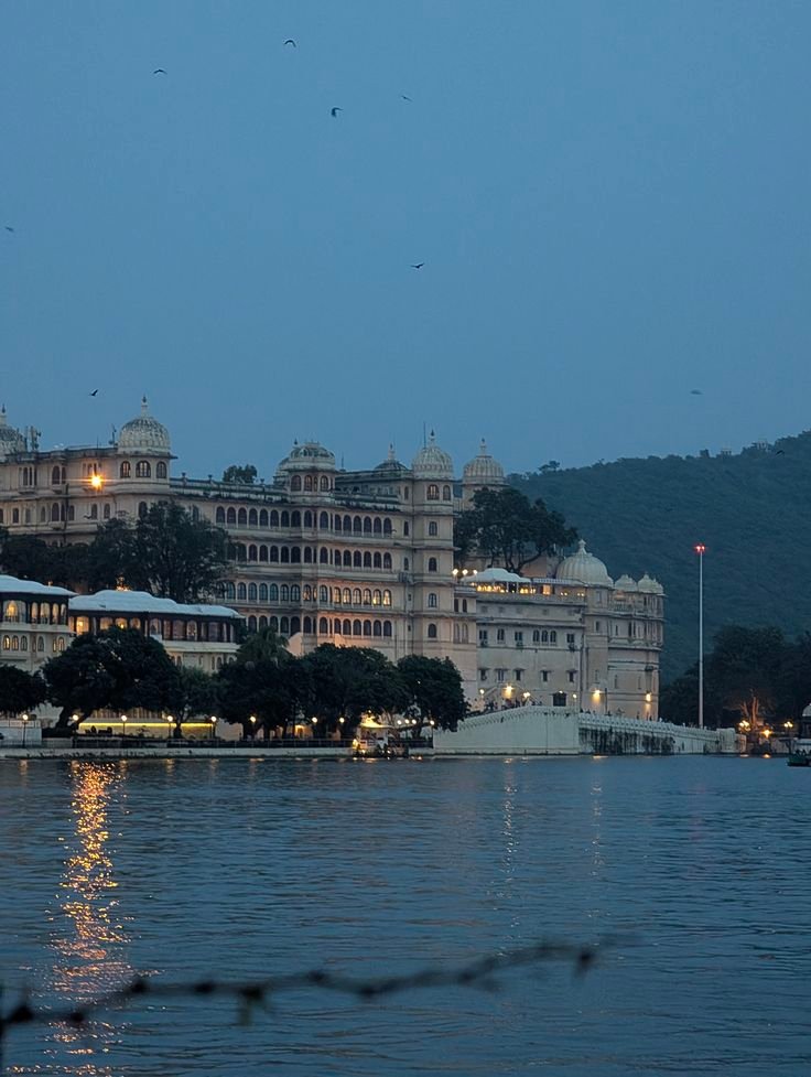 Illuminated City Palace at dusk reflecting on Lake Pichola in Udaipur, Rajasthan