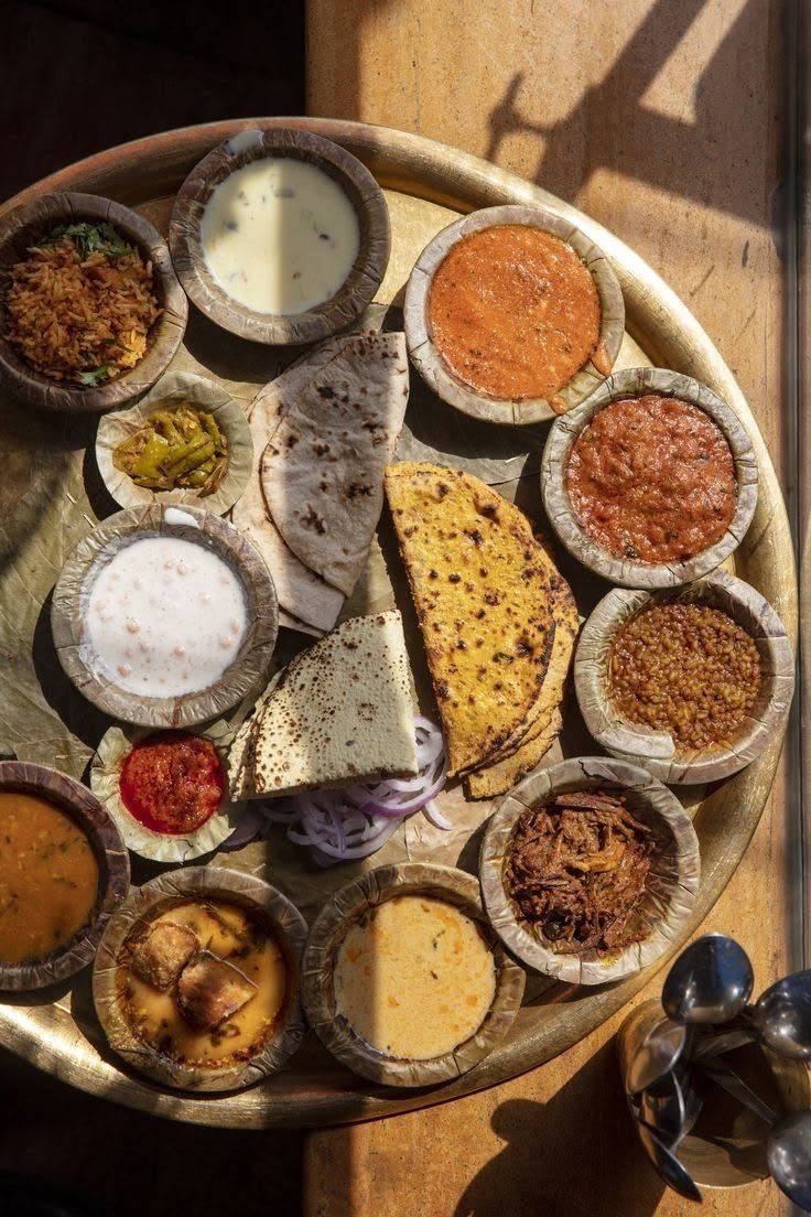 Traditional Rajasthani thali platter with assorted curries, dal, breads, and condiments served in leaf bowls on a brass plate