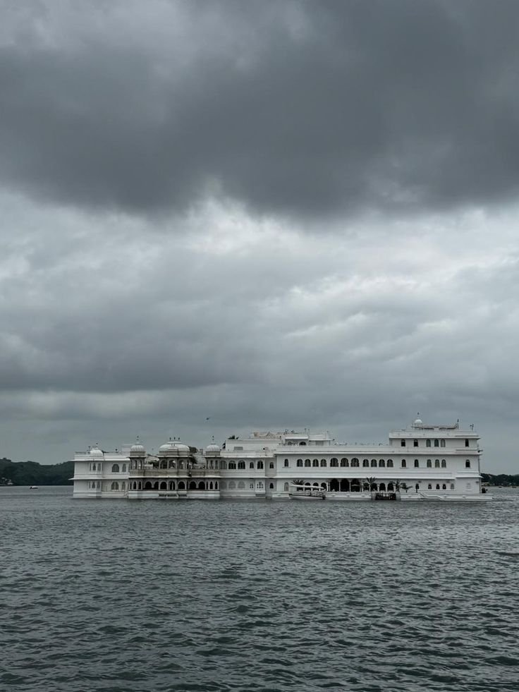 Lake Palace Udaipur surrounded by lake water under a cloudy sky
